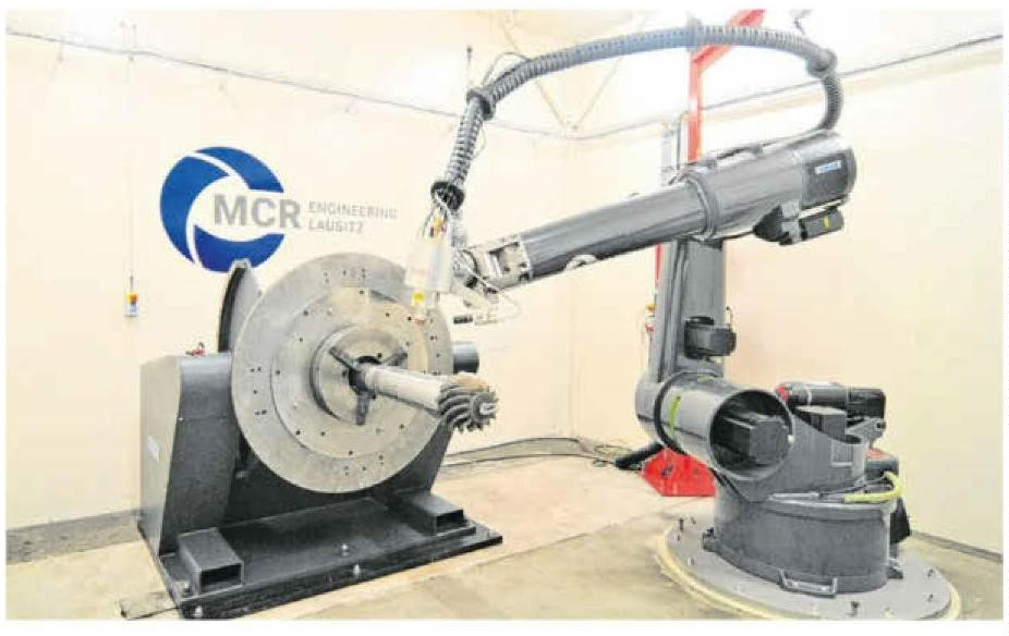 Der neue 3D-Metalldrucker in der LEAG-Hauptwerkstatt besteht unter anderem aus dem beweglichen Roboterarm sowie einem Laserkopf, in dem sechs Laser ringförmig verbaut sind.