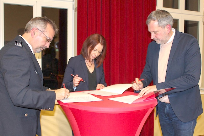 Oberbürgermeister Tobias Schick, der Präsident des Stadtfeuerwehrverbandes Jochen Schubert sowie Schulleiterin Grit Duschka setzen ihre Unterschriften unter die Vereinbarung.