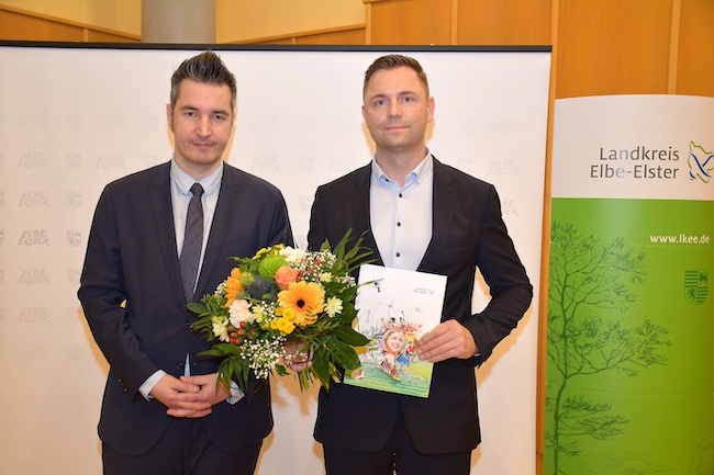 Kreistagsvorsitzender Dr. Sebastian Rick (l.) und Marcel Schmidt (r.) nach der Vereidigung mit Blumenstrauß und Urkundenmappe.