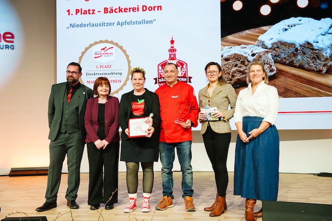 Auf der Bühne ausgezeichnet der Elbe-Elster Apfelstollen. Vlnr. Kai Rückewold Geschäftsführer von pro agro e.V., Andrea Opptiz vom Kerngehäuse e.V.; Daniela und Stefan Dorn von der Bäckerei Dorn; Hanka Mittelstädt, Ministerin für Landwirtschaft, Umwelt und Klimaschutz des Landes Brandenburg; sowie Dorothee Berger, Vorstandsvorsitzende von pro agro e.V.