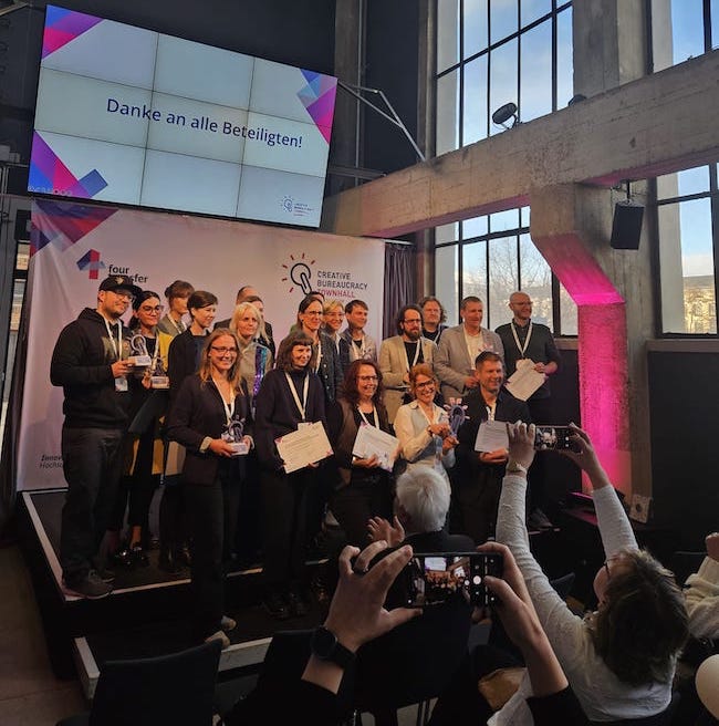 Zehn Ideen für eine bessere Verwaltung – alle Finalisten der Creative Bureaucracy Townhall Saxony mit Urkunden und Trophäen auf der Bühne im Kraftwerk Mitte Dresden.