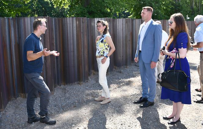 Gunnar Soyka, Projektleiter des Landesamtes für Umwelt Brandenburg, erläutert u.a. Umweltministerin Hanka Mittelstädt und Landrat Marcel Schmidt (v.l.n.r.) die laufenden Arbeiten an der Hochwasserschutzanlage entlang der Schwarzen Elster. Die mächtigen Spundwände verdeutlichen das Ausmaß der Baumaßnahme.